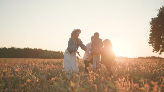 Cheerful young family of adult married couple parents and adorable two siblings running on wheat field, embracing together and laughing. Affectionate. Nature concept.