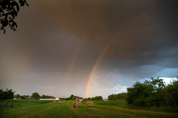 Rainbow over farm field of hay bales