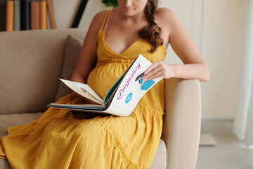 Close-up of young pregnant girl reading book about pregnancy during her maternity leave - obrazy, fototapety, plakaty