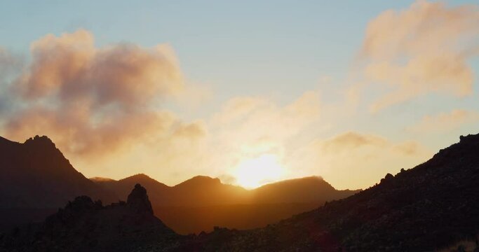 High deserted mountains at dusk or dawn. Sun rays illuminate rocks. Cloudy colourful sky in background. Teide national park, Tenerife. Canary islands.