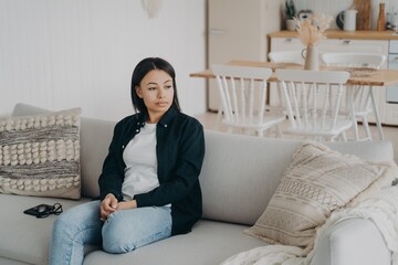 Pensive calm woman tired from homework or work day relax sitting on couch in living room at home