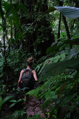 Naklejka na ściany i meble Tourist woman with backpack hiking in green tropical dark forest. Summer vacation in La Fortuna, Costa Rica.