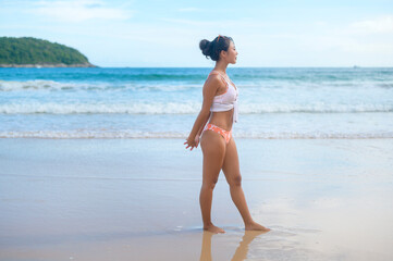 Fototapeta na wymiar Young asian woman in bikini doing yoga on the beach, health and meditation concept