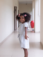 Portrait of cute little African girl with Afro hair style posing and looking at camera while walking in a walkway