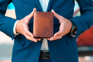 A businessman in an elegant blue suit shows off a brown handmade leather document holder. Close-up...
