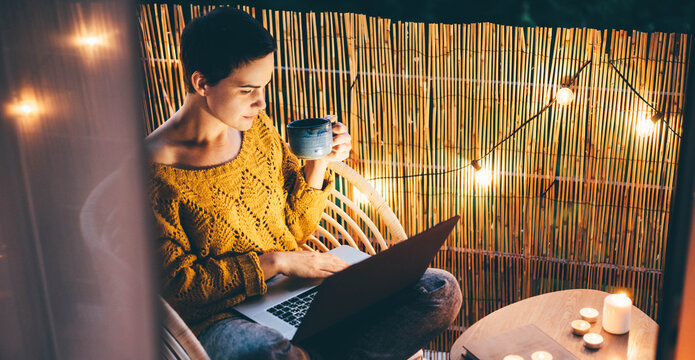  Woman using laptop at balcony of her apartment at the night.