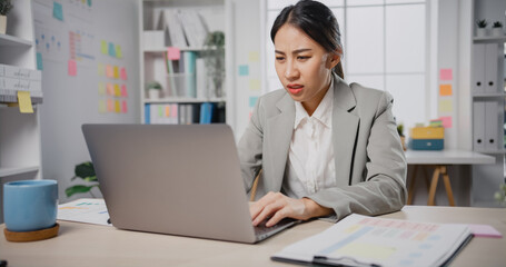 Young Asia businesswoman sitting on desk crazy with overworked stress angry massive work scream at...
