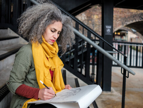 An iranian mature artist woman is making a draw sitting on stairs in London area.