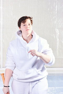 Natural portrait of young handsome transgender man posing with baseball bat. Caucasian with wavy brown hair. Wearing white hoodie and trousers.	