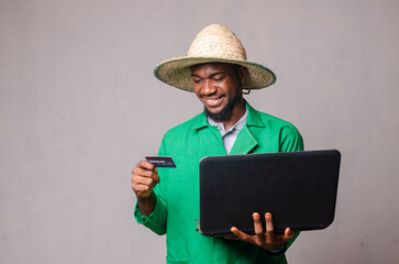 Young man with a cap holding a laptop computer and card smiling.