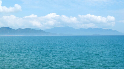   Sea with turquoise color water and blue sky with white clouds and the outlines of mountains on...