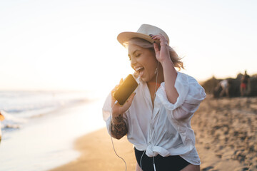 Excited female in earphones spending summertime at coastline beach - rejoicing on vacations, happy...