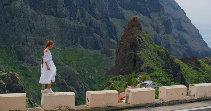 Attractive young woman in white dress walks in the mountains village Masca, green hills and rocks landscape, slow motion. Tenerife.