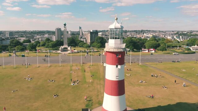 Aerial drone shot of a red and white striped lighthouse on the coast in Plymouth, UK