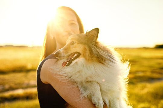 Woman with her dog during a golden sunset. Hugging fluffy sheltie.