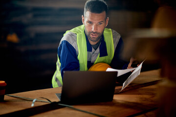 Warehouse foreman works on working on computer while analyzing reports at lumber department.