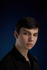 Portrait of a brunette teenager, in a black shirt on a navy blue background.