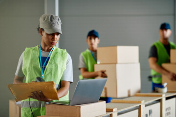 Black female worker scanning packages and using laptop while working at distribution warehouse.
