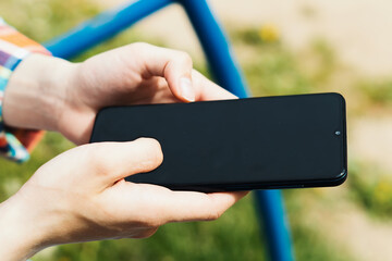 Women's hands hold a mobile phone with an empty black screen. A student girl is typing on a smartphone. A cell phone in the hands of a girl. Communication, development, training, entertainment online.