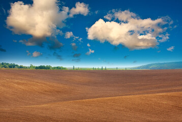 Plowed agricultural field soil on background of rural landscape and mystical sky with white clouds