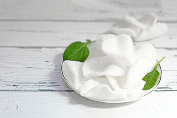 A pile of white fried Vietnamese rice chips on a platter on a white wooden board , close- up