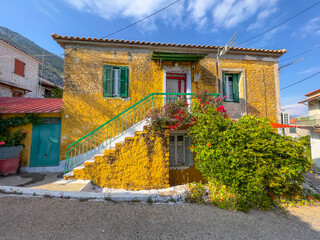 Facades of old and colorful houses in a fishing village in Greece. Old houses surrounded by green vegetation and colorful flowers. Building texture pattern.