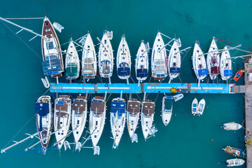 Aerial top-down view of docked sailboats. Top down view of yachts in the marina. Sailboats and regular Boats moured in Palairos Marina Greece. Sailboats and catamarans anchored in the harbour.