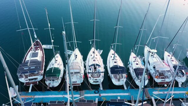 Aerial top-down view of docked sailboats. Top down view of yachts in the marina. Sailboats and regular Boats moured in Palairos Marina Greece. Sailboats and catamarans anchored in the harbour.