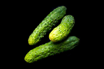 three green cucumbers lie on a black background