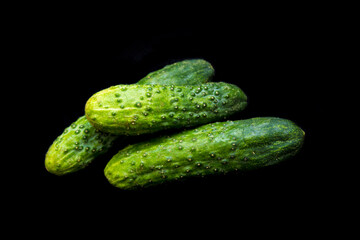 three green cucumbers lie on a black background
