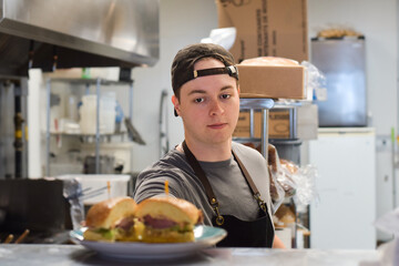 Restaurant kitchen employee placing plate with sandwich food order on kitchen window