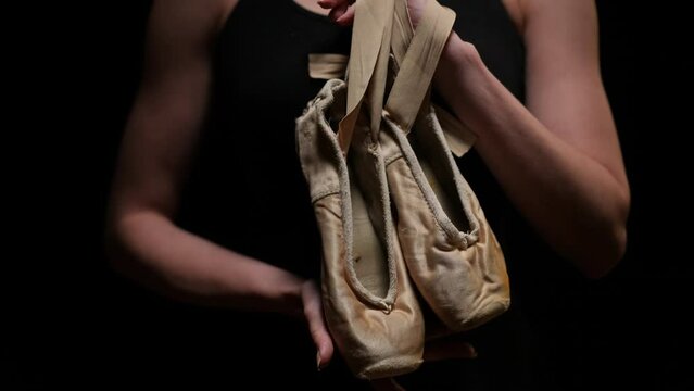 Close-up unrecognizable woman raising hand with pointies hanging on palm. Slim graceful skilled Caucasian ballerina posing at black background. Choreography concept
