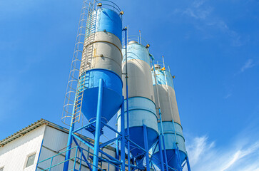 Large blue industrial tanks for cement, sand, water. Metal stairs leading to metal containers. Side view.