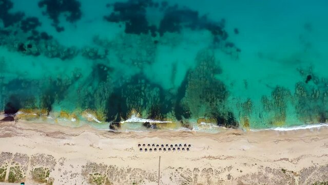 Umbrellas lined up on the sandy beach by the turquoise sea. Top view of a transparent blue sea with beautiful waves on the beach. Summer vibes concept. Exotic beach from above