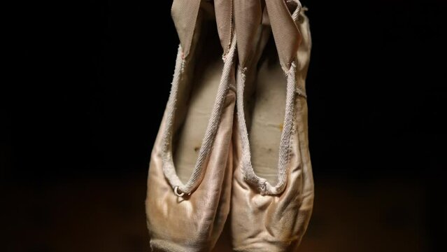 Close-up ballet pointies hanging at black background. Shoes for classic dancing closeup. Art and choreography