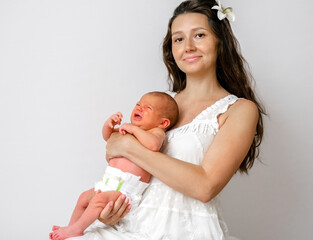 Beautiful confident young woman holding her new born baby on background on white wall. Happy young...