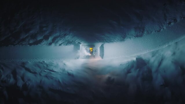 Aerial view snowcat rises up mountain. Bulldozer with turned on headlights removing snow from ski resort slope at dark night, Aspen Colorado 4K. Snow Grooming, Fix Trail on Ski Resort Slope at Night