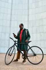 African businessman reading a message on his smartphone while standing outdoors with bike