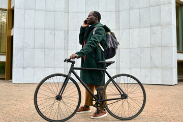 African businessman having a conversation on mobile phone while standing with his bike outdoors