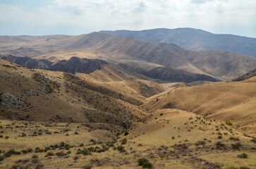 Autumn landscape of gentle slopes of mountainous terrain covered with trees and dry grass. Caucasus Mountains, Armenia
