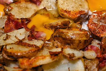 Russet potato with skin, bacon and eggs frying on the stove..