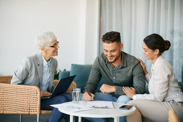 Happy couple singing contract with their financial advisor during meeting in the office.