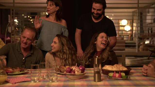 Group Of Happy Friends And Family Laughing And Smiling Around Table At Night In Home Backyard