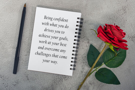 Motivational quote on note book with red roses and a pen.