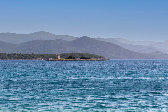 Coast in Croatia - pebble beach with beautiful blue sea in the background a small island with a church and beautiful mountains