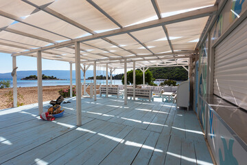 Beach bar with blue plank floor and white sunbeds and white fabric roof against blue sea background