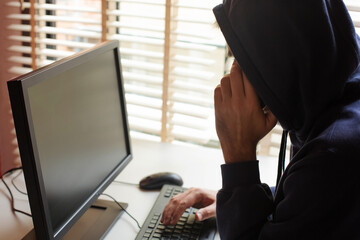 A hacker in a hooded sweatshirt with a hidden face typing on a computer keyboard and talking on a...