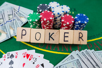 The word poker on wooden cubes, poker chips with playing cards on the green casino table.