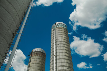 Three concrete grain silos against a blue sky and clouds.  Access to grains is difficult causing food shortages and high inflation around the world. 