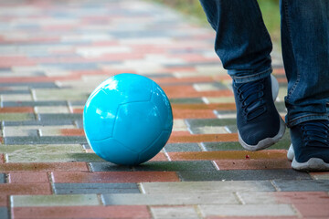 Man legs in blue jeans and blue shoes kicking the blue ball on the ground